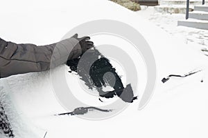 Woman cleaning car from snow with hand in glove. Snow-covered car windshield. parked car covered with snow during snowing in