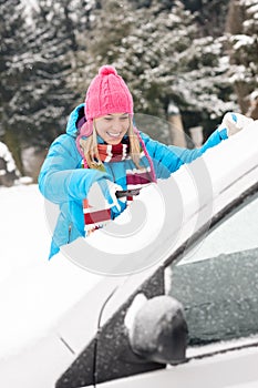 Woman cleaning car windshield of snow winter