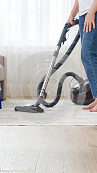 Woman cleaning the carpet with vacuum cleaner in the living room