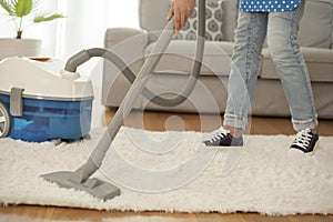 Woman cleaning carpet with a vacuum cleaner in room