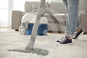 Woman cleaning carpet with a vacuum cleaner in room