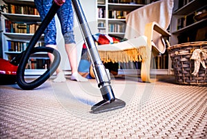 woman cleaning carpet with a vacuum cleaner in room - focus on h