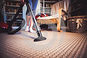 woman cleaning carpet with a vacuum cleaner in room - focus on h