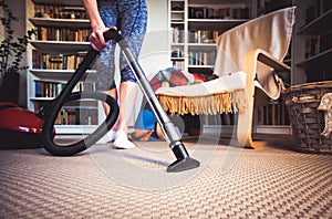 woman cleaning carpet with a vacuum cleaner in room - focus on h