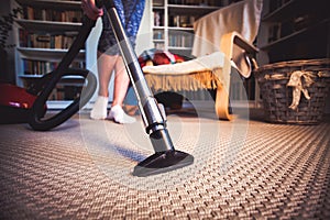 woman cleaning carpet with a vacuum cleaner in room - focus on h