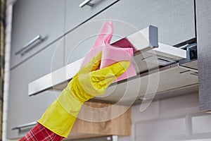 Woman Cleaning Cooker Hood With Rag In Kitchen. Close up of hand in protective gloves clean the metal extractor hood