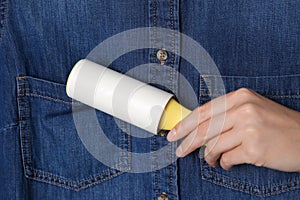 Woman cleaning denim shirt with lint roller, closeup