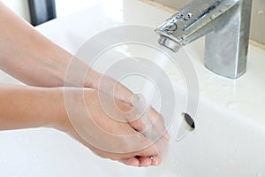 The woman cleaning dirty hands by washing hand with foam soap and water in white sink in bathroom