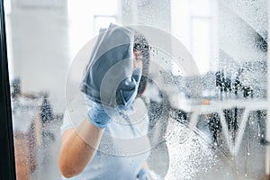 Woman cleaning dirty window by using towel. View through the glass