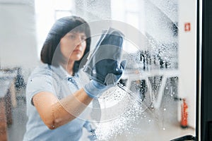 Woman cleaning dirty window by using towel. View through the glass