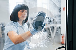 Woman cleaning dirty window by using towel. View through the glass