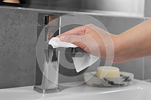 Woman cleaning faucet of bathroom sink with paper towel, closeup