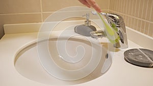 Woman is cleaning faucet and sink with brush, hand closeup.