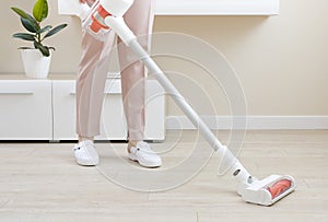 Woman cleaning floor with wireless vacuum cleaner in living room