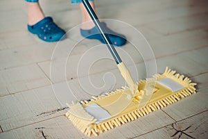 Woman cleaning floor with yellow mop at home. Microfiber mop isolated on white wooden floor background, closeup, indoors