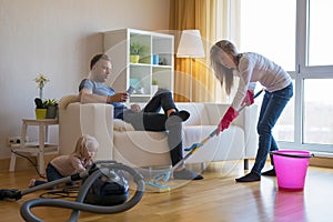 Woman cleaning floors at home while her lazy man sitting in couch photo