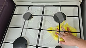 Woman cleaning a gas stove with yellow cloth