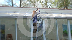 Woman cleaning glass house roof with high pressure tool in nature.