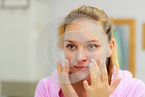 Woman cleaning her face with scrub in bathroom.