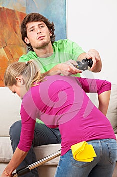 Woman cleaning the house and her husband with console