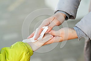 Woman cleaning kid hands with antiseptic tissue outdoors. Hands hygiene. Female using a antibacterial wet napkin wipe