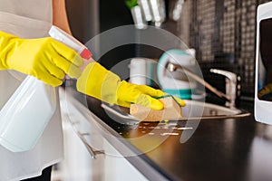 Woman cleaning kitchen cabinets with sponge and spray cleaner