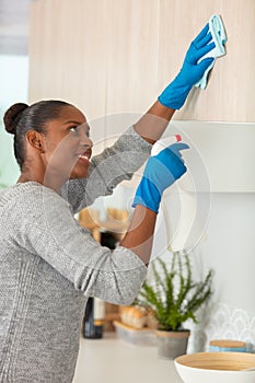 woman cleaning kitchen cupboards with detergent spray