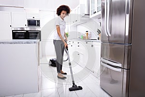 Woman Cleaning Kitchen Floor With Vacuum Cleaner