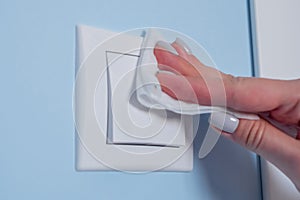 Woman cleaning light switch on blue wall with wet wipe - disinfection concept