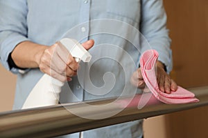 Woman cleaning metal railing with rag and spray detergent, closeup