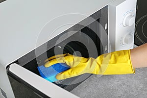 Woman cleaning microwave oven with sponge in kitchen