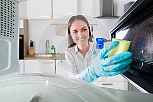 Woman Cleaning Microwave With Spray Bottle And Sponge