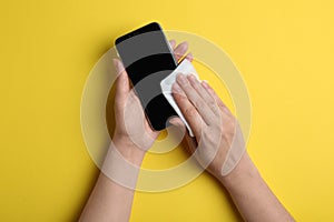 Woman cleaning mobile phone with antiseptic wipe on background, top view