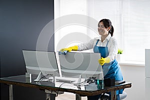 Woman Cleaning Office Desk And Computer Monitor