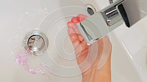 Woman cleaning purple glitter of washbasin in bathroom and polluting clean water by toxic plastics
