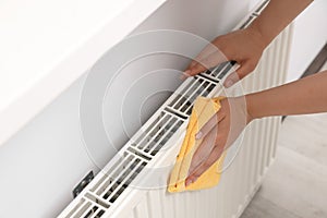 Woman cleaning radiator with rag indoors, closeup