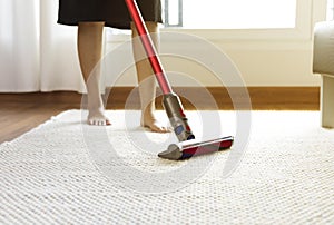 Woman cleaning rug carpet with vacuum cleaner at home