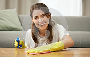 Woman, cleaning and table in home with smile for housework, spray and cloth for furniture. Female cleaner, or worker