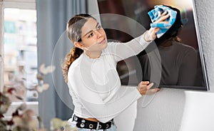 Woman cleaning TV with rag at home