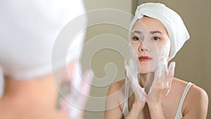 Woman cleaning washing her face with foam in bathroom