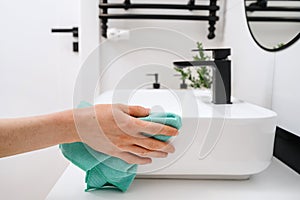 Woman cleaning white washbasin with a cloth photo