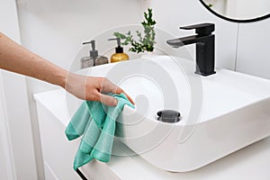 Woman cleaning white washbowl with a black tap in bathroom photo