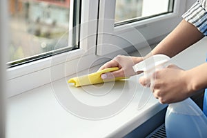 Woman cleaning window sill with rag and detergent indoors