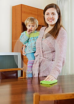 Woman cleaning wooden furiture with rag at home