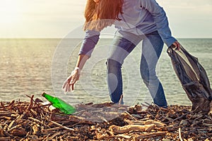 Woman cleans garbage on the beach, picks up the bottle. Ecology, earth day, cleaning of the territory concept. Light from the sky