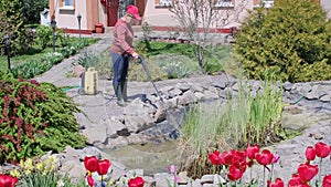 Woman cleans garden pond bottom from dirt and silt with high-pressure washer