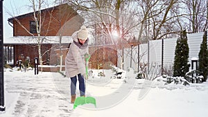 A woman cleans the path near the house from heavy snow. A shovel in hands.
