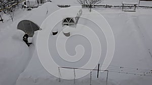 A woman cleans the path to the greenhouse from snow. Greenhouses in the snow top view