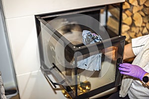 The woman cleans soot from the fireplace glass door using paper.