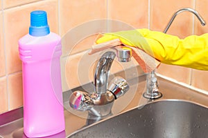 woman cleans the tap in the kitchen with a rag, hands in yellow gloves